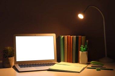 Geceleri dizüstü bilgisayarı, kırtasiyesi ve parlayan lambası olan işyeri