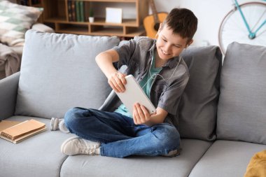 Genç çocuk oturma odasındaki kanepede tabletle oyun oynuyor.