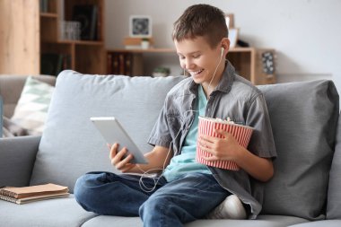 Tabletli ve patlamış mısırlı genç çocuk oturma odasındaki kanepede film izliyor.