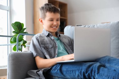 Genç çocuk oturma odasındaki kanepede dizüstü bilgisayar kullanıyor.