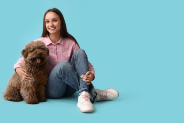 Genç bir kadın sevimli kahverengi kaniş köpeğine sarılıyor ve mavi arka planda oturuyor.