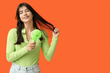 Turuncu arka planda mini fanı olan genç bir kadın.