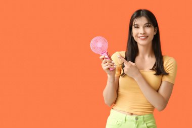 Turuncu arka planda mini fanı olan genç bir kadın.