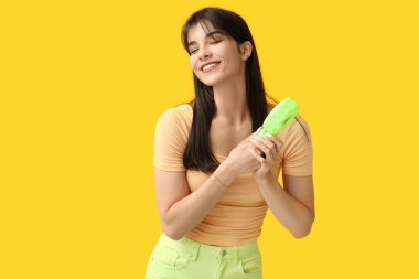 Sarı arka planda mini fanı olan genç bir kadın.