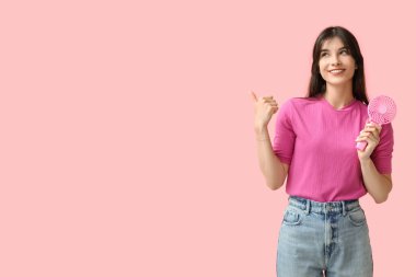 Mini fanı olan genç bir kadın pembe arka plandaki bir şeyi işaret ediyor.