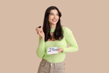 Bej arka planda bir kutu lezzetli çikolata şekeri olan mutlu genç bir kadın.