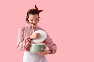 Pembe arka planda tenceresi olan güzel, genç, mutlu bir ev kadını.