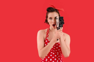 Kırmızı arka planda retro kameralı güzel, genç, şok olmuş ev hanımı.