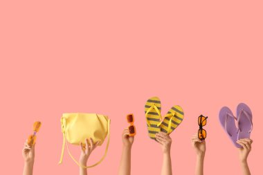 Şık güneş gözlüklü kadın elleri, pembe arka planda çanta ve parmak arası terlikler.