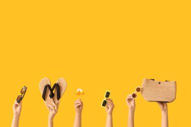 Şık güneş gözlüklü kadın elleri, hasır çanta, parmak arası terlikler ve sarı arka planda mini şemsiye.