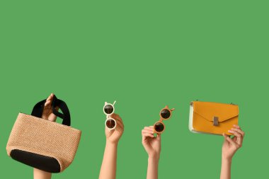 Şık güneş gözlükleri ve yeşil arka planda çantaları olan kadın elleri.