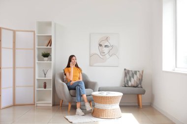 Odadaki koltukta otururken cep telefonu kullanan genç bir kadın.