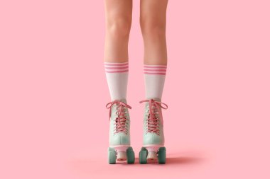 Pembe arka planda paten giyen genç kadınların bacakları.