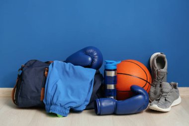 Boks eldivenleri, spor çantası, su şişesi, spor giysileri ve mavi duvarın yanında ayakkabılar.