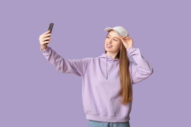 Beyaz şapkalı güzel bir kadın leylak arkaplanda selfie çekiyor.