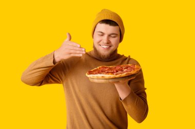 Sarı arka planda lezzetli pepperoni pizzalı genç adam.