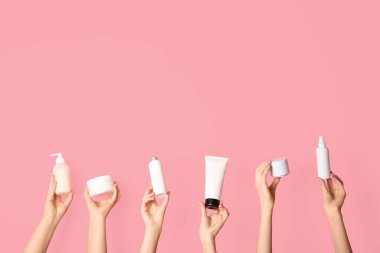 Pembe arka planda kavanozlu kadın elleri ve kozmetik ürünleri şişeleri