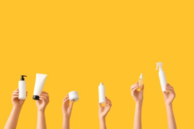 Kavanoz, tüp ve turuncu arka planda kozmetik ürünleri olan kadın elleri