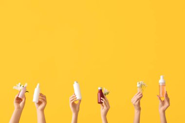 Turuncu arka planda kozmetik ürünler ve çiçeklerle dolu kadın elleri