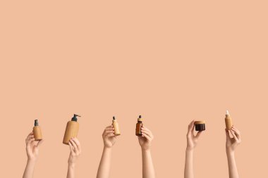 Kavanozlu kadın elleri ve kahverengi arka planda farklı kozmetik ürünleri şişeleri.