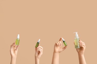 Kahverengi arka planda kozmetik ürünleri olan kadın elleri