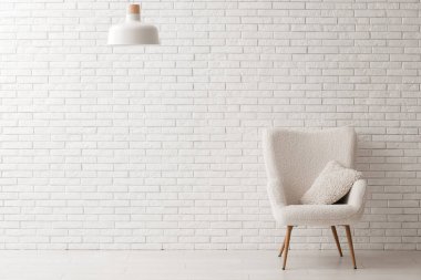 Yastıklı koltuk ve lamba beyaz tuğla duvarın yanında.