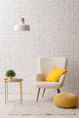 Sarı yastıklı koltuk, puf ve beyaz tuğla duvarın yanındaki sehpa.