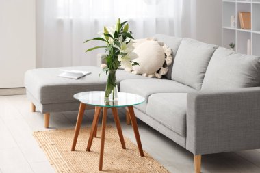 Kahve masasında gri kanepe, yastık ve nilüfer çiçeği vazosu olan şık bir oturma odası.