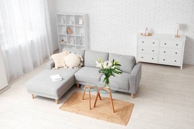 Kahve masasında gri kanepe, yastık ve nilüfer çiçeği vazosu olan şık bir oturma odası.