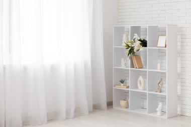 Salonda beyaz tuğla duvarın yanında nilüfer çiçekleri olan raf ünitesi.