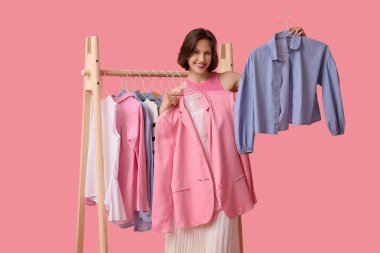 Güzel, genç bir kadın pembe arka planda kıyafet seçiyor.