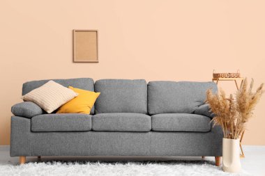 Gri kanepe ve vazo bej duvarın yanında otla süslenmiş vazo