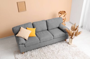 Aydınlık oturma odasının içinde şık gri bir kanepe ve otlar var.