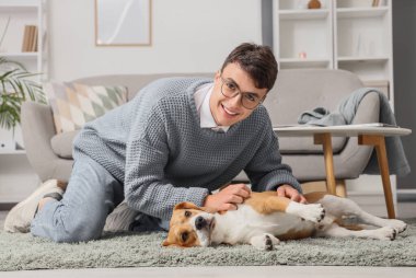 Gözlüklü genç adam evde yerde sevimli Beagle köpeğiyle oynuyor.