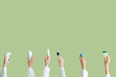 Yeşil arka planda termometresi, hapları, lavmanı ve glukometresi olan kadın elleri