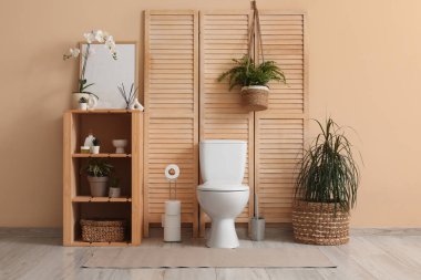 Seramik klozet, raf ünitesi ve bitkilerle dolu modern tuvalet.