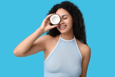 Mavi arka planda taze hindistancevizi olan güzel bir Afro-Amerikalı kadın.