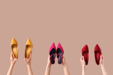 Bej arka planda farklı topuklu ayakkabı tutan kadın eller.