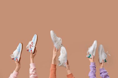 Bej arka planda farklı spor ayakkabıları olan kadın elleri.