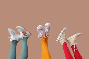 Bej arka planda farklı spor ayakkabıları olan kadın bacakları.