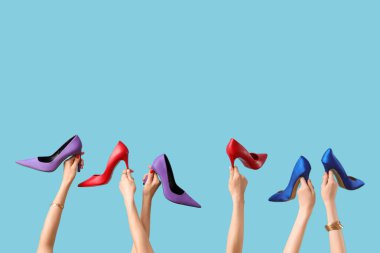 Mavi arka planda farklı topuklu ayakkabı tutan kadın eller.