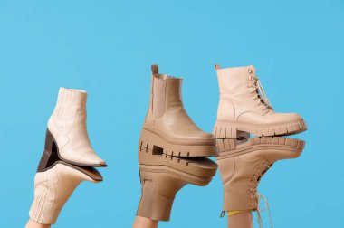 Mavi arka planda farklı çizmeleri olan kadın bacakları.