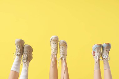Sarı arka planda farklı spor ayakkabıları olan kadın bacakları.