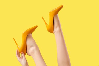 Sarı arka planda topuklu kadın bacakları.