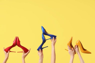 Sarı arka planda farklı topuklu kadın elleri.