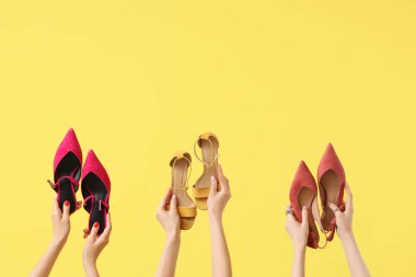 Sarı arka planda farklı topuklu ve sandaletli kadın elleri.