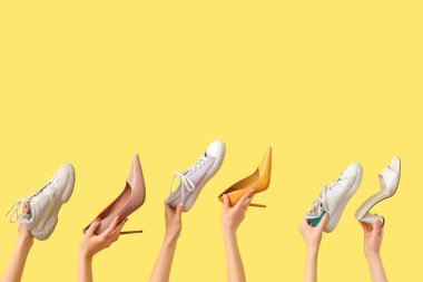 Farklı spor ayakkabıları ve sarı arka planda topuklu ayakkabıları olan kadın elleri.