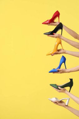 Sarı arka planda farklı topuklu ayakkabı tutan kadın eller.