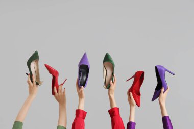 Gri arka planda farklı topuklu ayakkabı tutan kadın eller