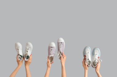 Gri arka planda farklı spor ayakkabıları tutan kadın eller.